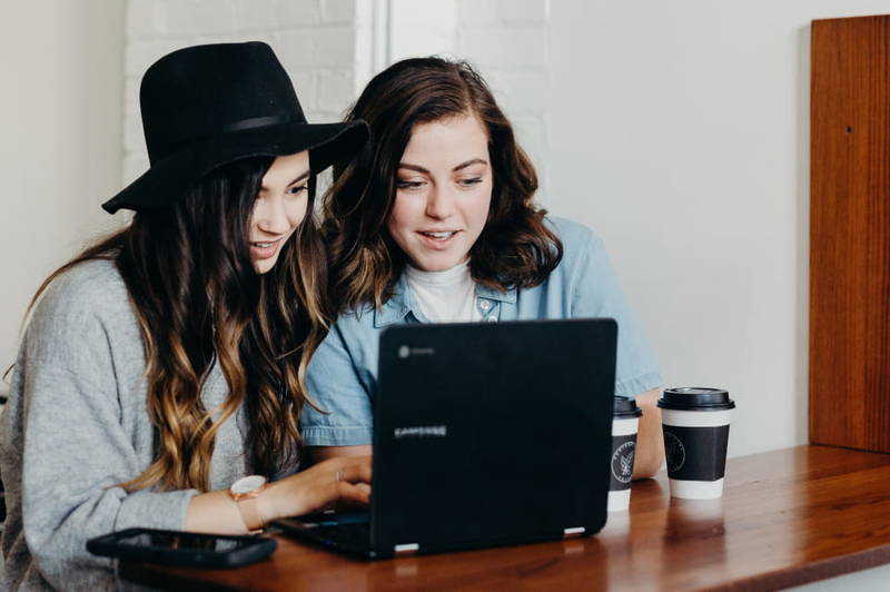 two girls in front of a laptop, having coffees